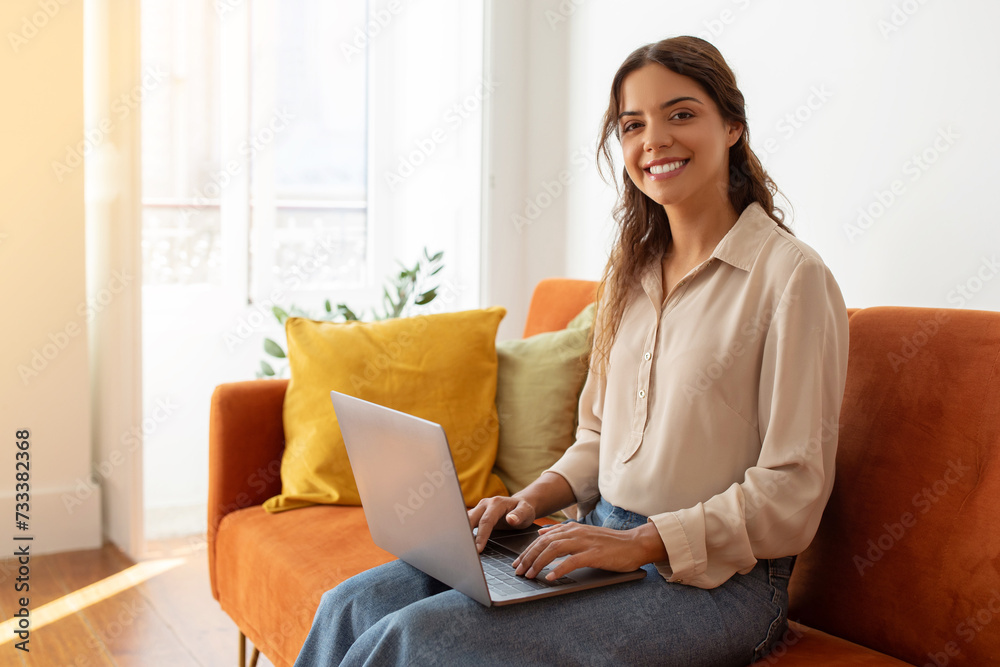 Young woman with laptop working from home, sitting on couch and smiling Young woman with laptop working from home, sitting on couch and smiling