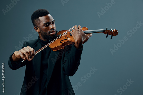 African American man in black suit playing violin, creating soulful music on gray background