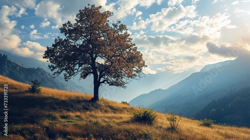 A majestic solitary tree with vibrant autumn foliage stands prominently in the foreground of a pastoral landscape. The hill it rests upon glows with a golden hue as it slopes down towards a valley. La