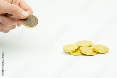 Male hand holding chocolate coin, stack of coins in the background isolated on white background, copy space photo