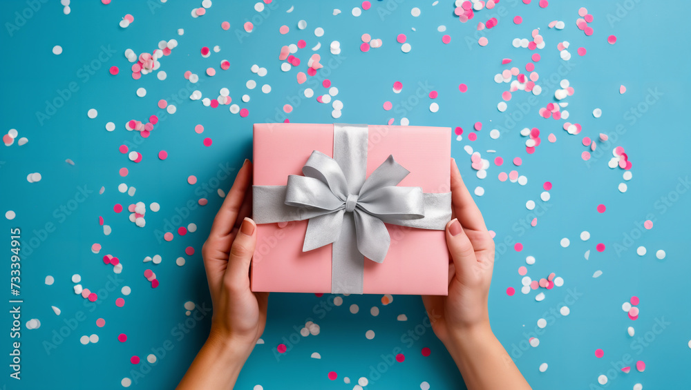 Women's hands holding elegant pink gift with silver ribbon on solid background with confetti. A gift, for example, for Mother's Day, Valentine's Day, birthday, Christmas, New Year, or Father's Day Women's hands holding elegant pink gift with silver ribbon on solid background with confetti. A gift, for example, for Mother's Day, Valentine's Day, birthday, Christmas, New Year, or Father's Day
