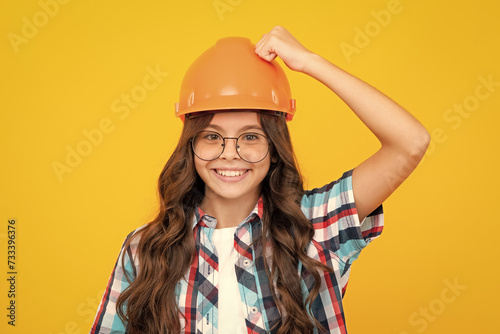 Close up portrait of teenager child builder in helmet. Teenage girl on repairing work isolated on yellow background.
