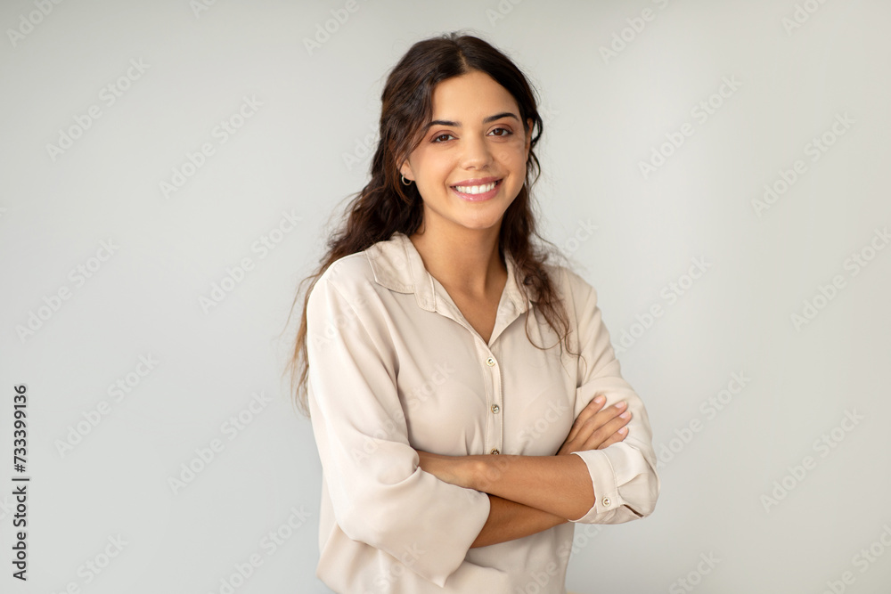 Smiling young woman standing confidently with arms crossed over light background Smiling young woman standing confidently with arms crossed over light background