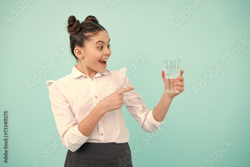 Teenager girl drinking water from glass on blue background. Daily life health. Drink water for health care and body balance. Thirsty kid, dehydration.