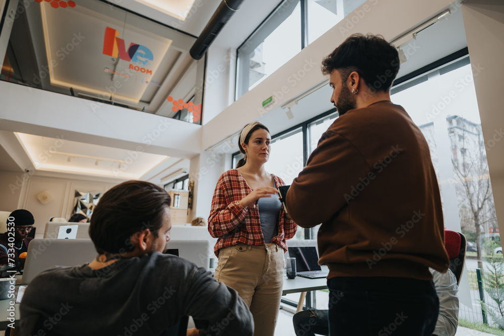 Fototapeta premium Two professionals casually interacting with each other in a bright, contemporary office space, with co-workers in the background.