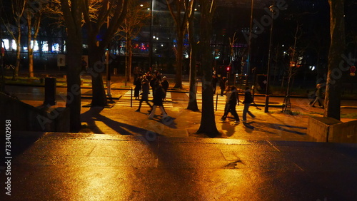 Grande rue ou avenue parisienne la nuit, ciel nuit noir, éclairage de lampadaires et réflexion de lumière sur surface eau et mouillée, promenade urbaine nocturne, circulation de voitures et de passant photo