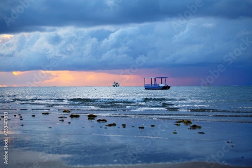 Early morning first sun light  on the beach. Blue sunrise on Japarating, Alagoas, Brazil. Fishng boats parked on water, small waves crashing the water edge, cloudy blue sky.