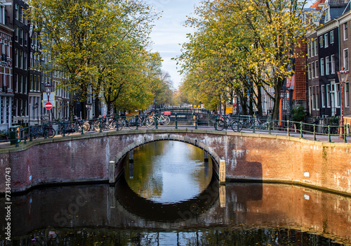 Peaceful morning of Amsterdam in the autumn with canal, bridge, buildings, bikes and trees.