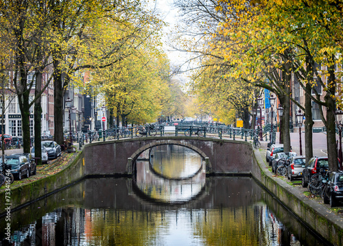 Peaceful morning of Amsterdam in the autumn with canal, bridge, buildings, bikes and trees.