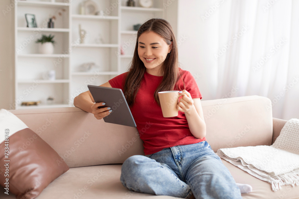 Relaxed young asian woman holding digital tablet and coffee mug Relaxed young asian woman holding digital tablet and coffee mug