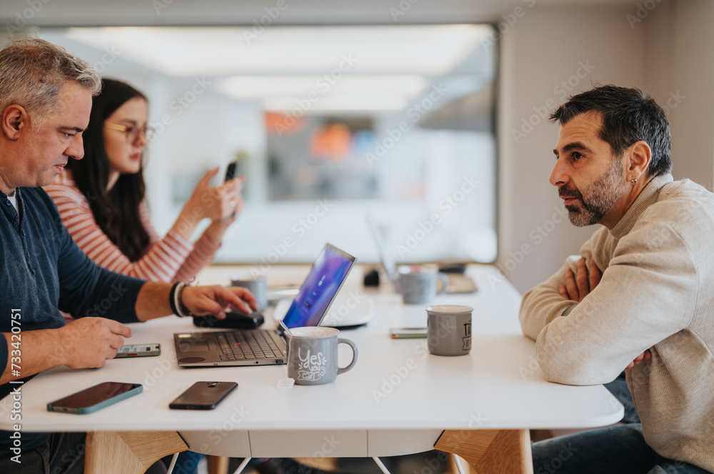A group of focused colleagues in a modern office setting, engaged in a casual meeting with laptops, smart phones, and coffee. A group of focused colleagues in a modern office setting, engaged in a casual meeting with laptops, smart phones, and coffee.