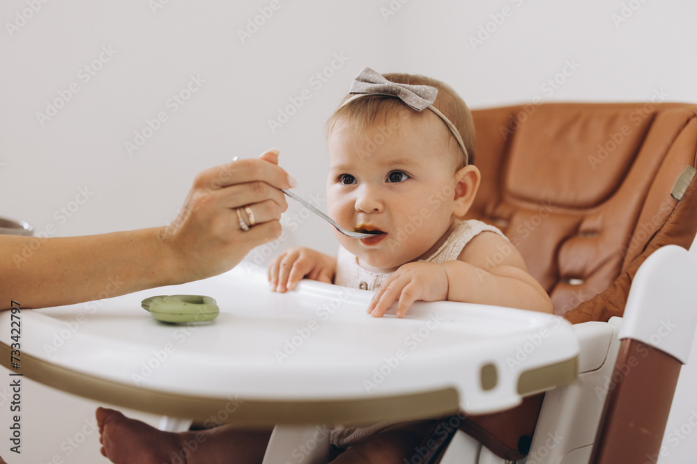 Mother feeding healthy food to her adorable little daughter sitting in high chair Mother feeding healthy food to her adorable little daughter sitting in high chair