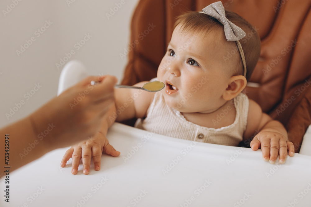 Mother feeding healthy food to her adorable little daughter sitting in high chair Mother feeding healthy food to her adorable little daughter sitting in high chair