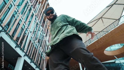 Low angle view of hipster pose in hip hop style surrounded by mall view. Portrait of sporty asian hip hop choreographer dancing break dance while looking at camera. Outdoor sport 2024. Endeavor.