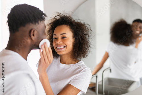 Happy African American couple engages in facial skincare in bathroom