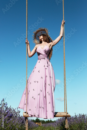 Young sexy beautiful woman swinging on hanging vintage swing in a lavender field against the background of the sky. 