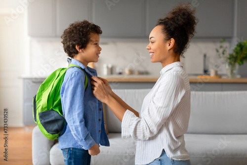 Happy black mother preparing child boy with backpack for school photo