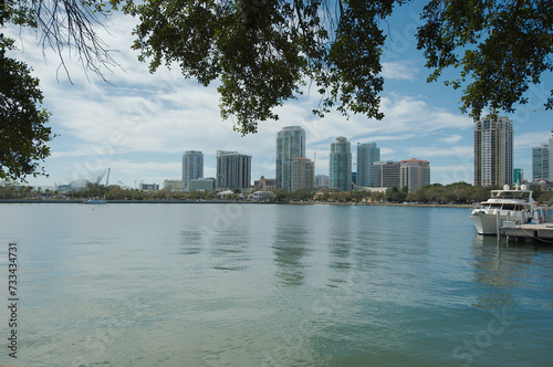 Cityscape of water with tall buildings on a sunny day with boats in the foreground. With a blue sky on a sunny day at the Vinoy  Basin waterfront in St. Petersburg  Florida. Trees in foreground top.