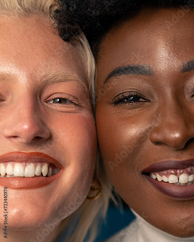Cheerful young women with different skin tones smiling at camera while standing together. Close up photo of a two interracial women standing face to face in a studio. Headshot of a two diverse women.
