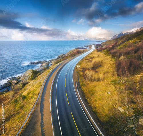 Aerial view of bridge, car, sea with waves and rocks at sunset