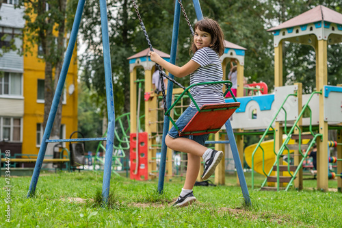 joyful smiling teenager girl 11 years old rides on a swing on the playground looks at the camera close-up. High quality photo