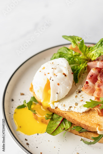 Toasts sandwich with poached egg, arugula, bacon and cream cheese on white plate marble background