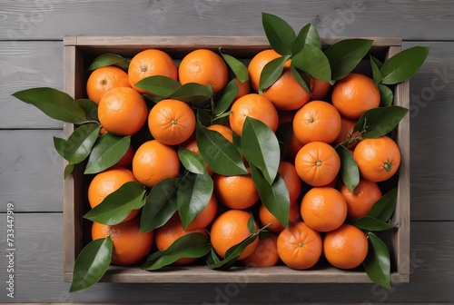Crate of ripe red oranges and green leaves on grey wooden table, top view
