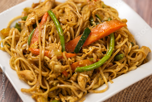 Delicious fried noodle served in the white plate on the Wooden background,Chinese noodle dishes of noodles,Noodles with chicken, green beans and carrots