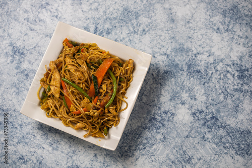 Delicious fried noodle served in the white plate on the marable background,Chinese noodle dishes of noodles,Noodles with chicken, green beans and carrots photo