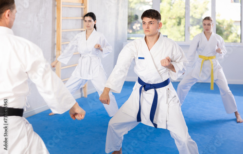 Active middle-aged guy wearing kimono training karate techniques in group during workout session