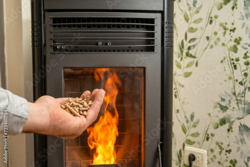 Man's hand holding pellets in front of the glass of a stove with a beautiful flame, sustainable and ecological heating photo