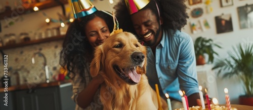 A man and woman are celebrating a birthday with their dog, a happy carnivore companion dog. The dog breed wags its tail, wearing a hat, making everyone smile and have fun.