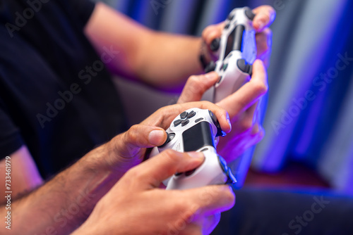 Close up of photo in holding joystick, playing video game or online streamer with friends in neon blue light curtain background. Concept of sitting couch lifestyles gamer in living room. Sellable.