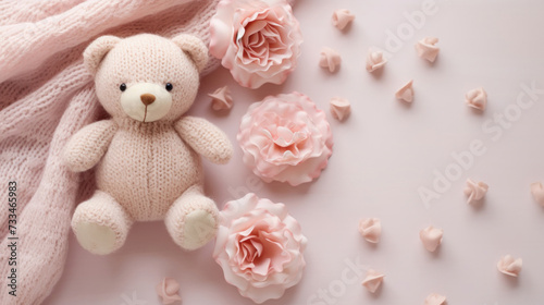 A small knitted amigurumi bear toy on a pink blanket, on a white background with flowers. Flat lay, top view, copy space. space for text