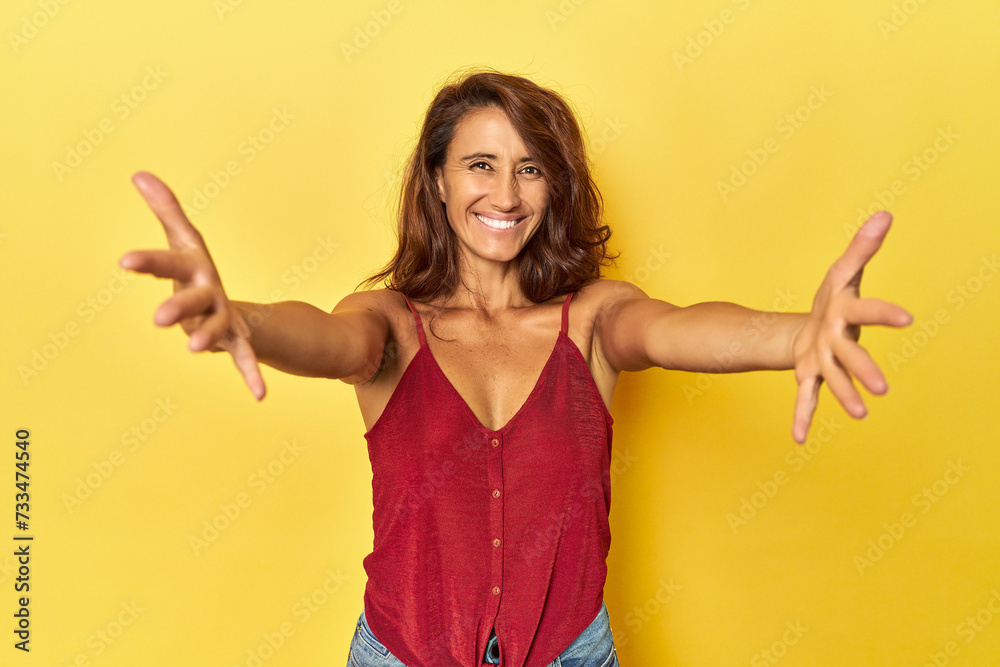Middle-aged woman on a yellow backdrop feels confident giving a hug to the camera. Middle-aged woman on a yellow backdrop feels confident giving a hug to the camera.