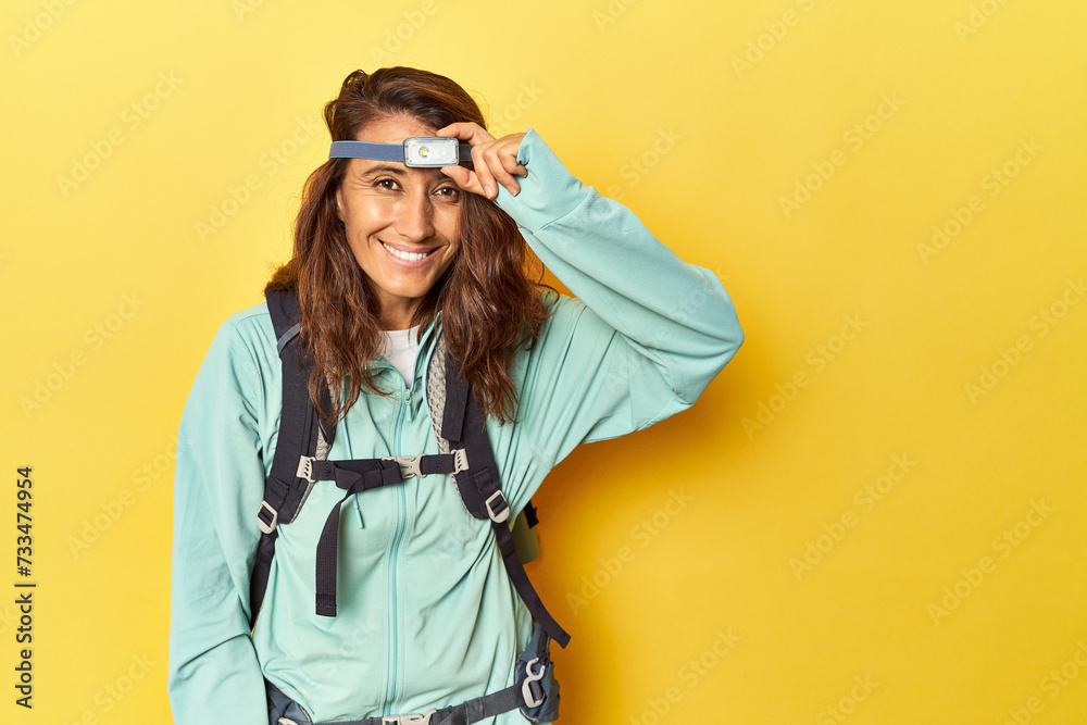 Middle aged hiker woman with backpack and frontal light on yellow - obrazy, fototapety, plakaty 