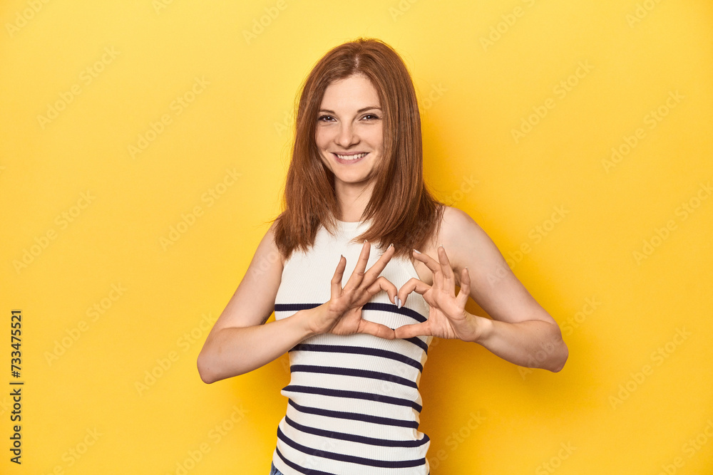 Redhead in a tank top, casual studio shot smiling and showing a heart shape with hands. Redhead in a tank top, casual studio shot smiling and showing a heart shape with hands.