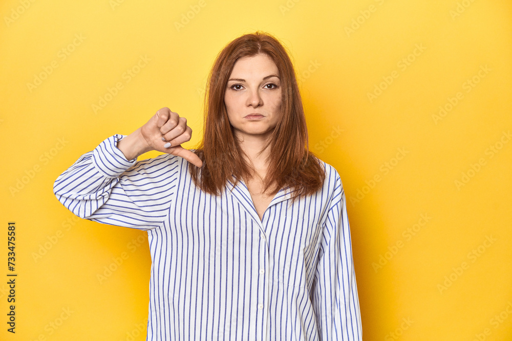 Business-dressed redhead, formal studio shot showing a dislike gesture, thumbs down. Disagreement concept. Business-dressed redhead, formal studio shot showing a dislike gesture, thumbs down. Disagreement concept.