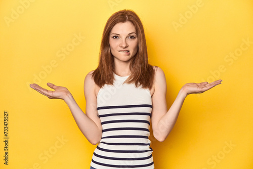 Redhead in a tank top, casual studio shot confused and doubtful shrugging shoulders to hold a copy space.