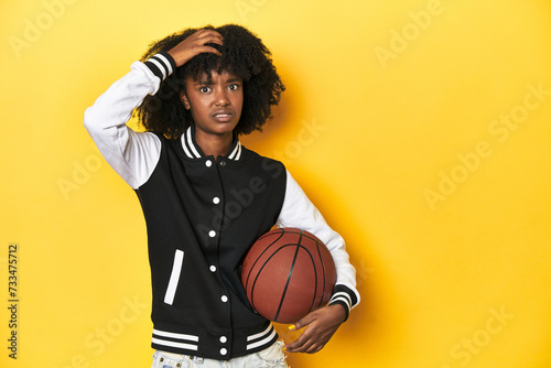 Vibrant teen girl with basketball on yellow studio background being shocked, she has remembered important meeting.