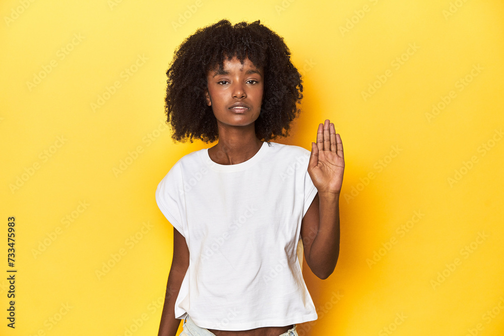 Teen girl in white tank top, yellow studio background smiling cheerful showing number five with fingers. Teen girl in white tank top, yellow studio background smiling cheerful showing number five with fingers.