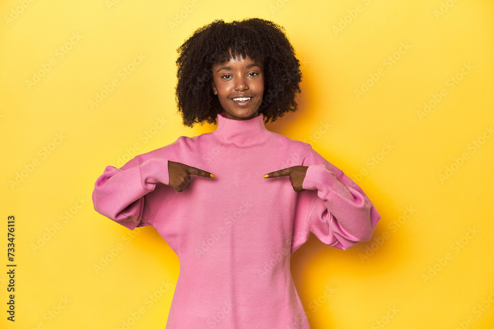 Teen girl in pink sweatshirt, yellow studio backdrop surprised pointing with finger, smiling broadly. Teen girl in pink sweatshirt, yellow studio backdrop surprised pointing with finger, smiling broadly.