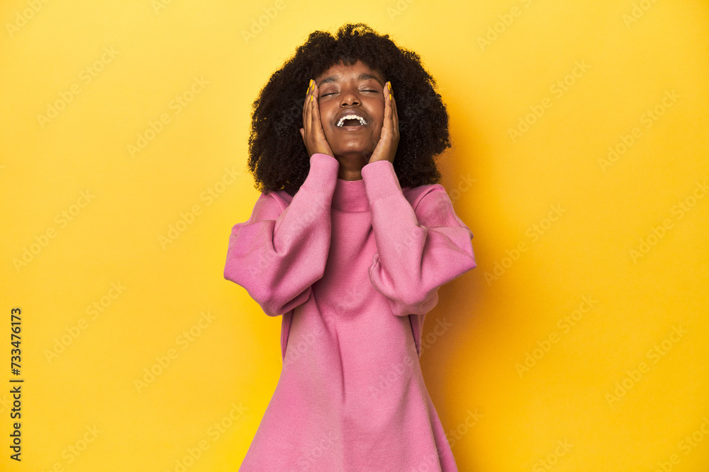 Teen girl in pink sweatshirt, yellow studio backdrop laughs joyfully keeping hands on head. Happiness concept. Teen girl in pink sweatshirt, yellow studio backdrop laughs joyfully keeping hands on head. Happiness concept.