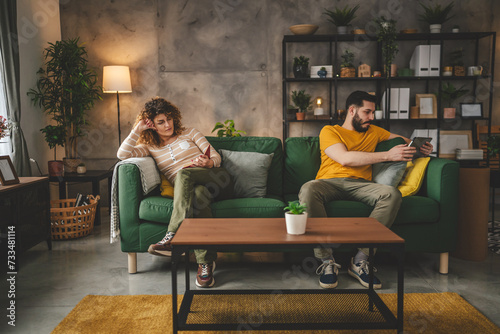 man and woman read book and use digital tablet at home on sofa bed photo