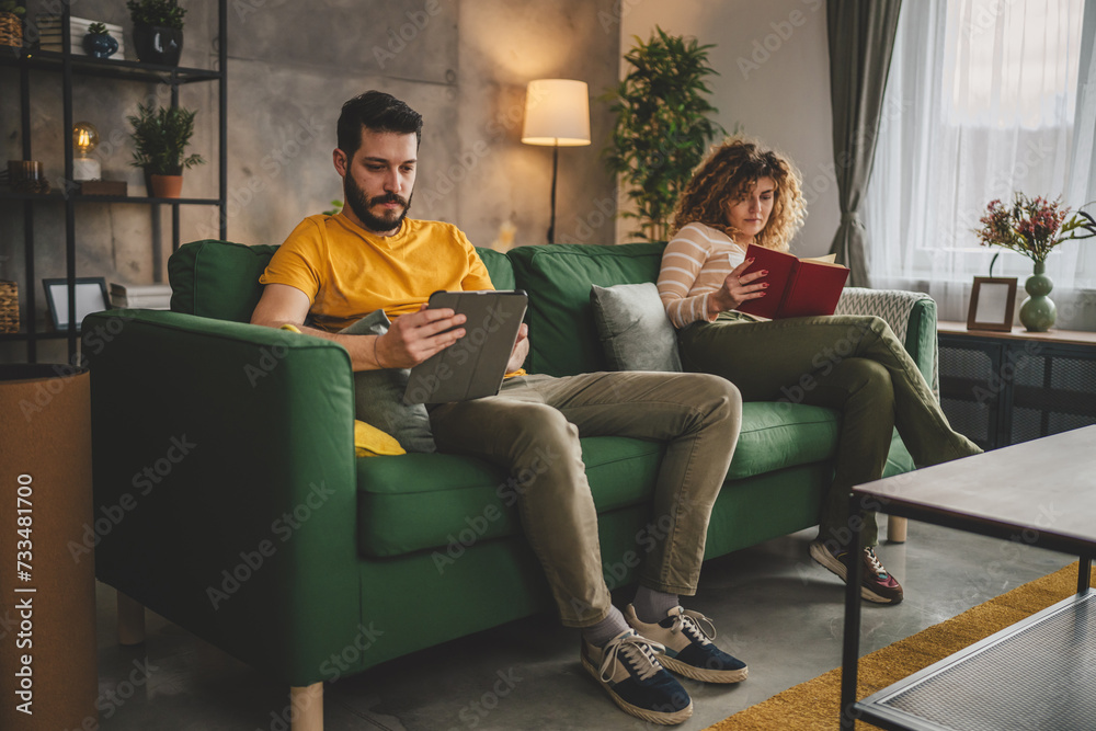 man and woman read book and use digital tablet at home on sofa bed man and woman read book and use digital tablet at home on sofa bed