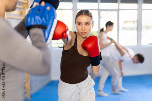 Young woman and adult man in boxing gloves doing boxing in gym.. © JackF