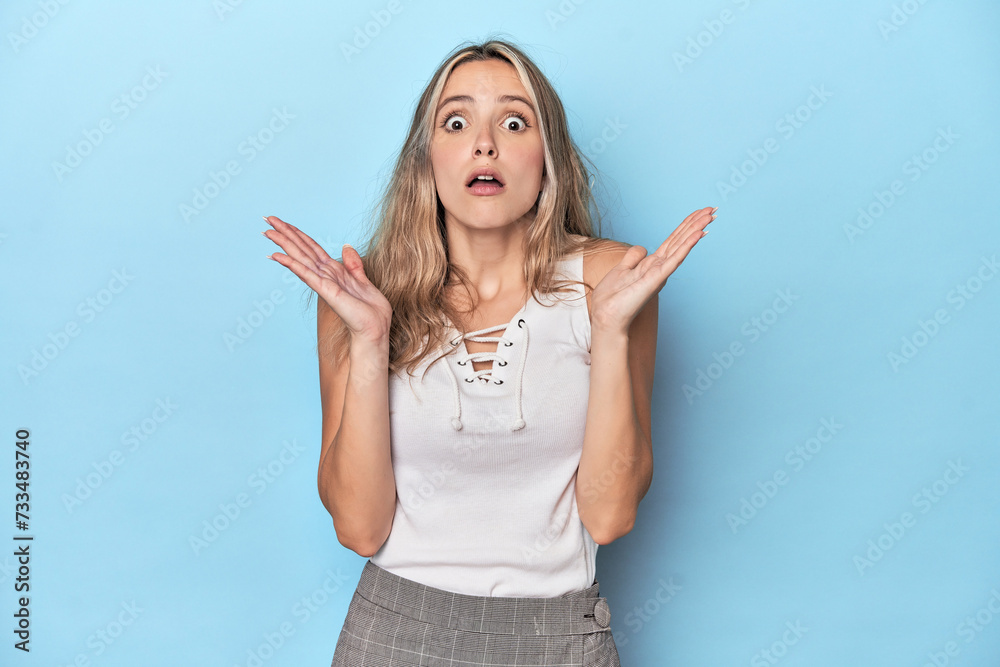 Fototapeta premium Blonde young caucasian woman in blue studio surprised and shocked.