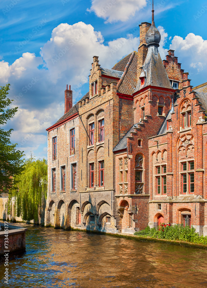 Medieval town Bruges in Belgium. Panorama and landscape vintage channel with old bruges brick houses broach on roof. Sunny day Brugge blue sky, clouds green trees. Europe travel destination
