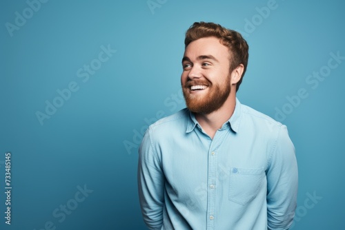 Portrait of a happy young bearded man standing against blue background. © Iigo