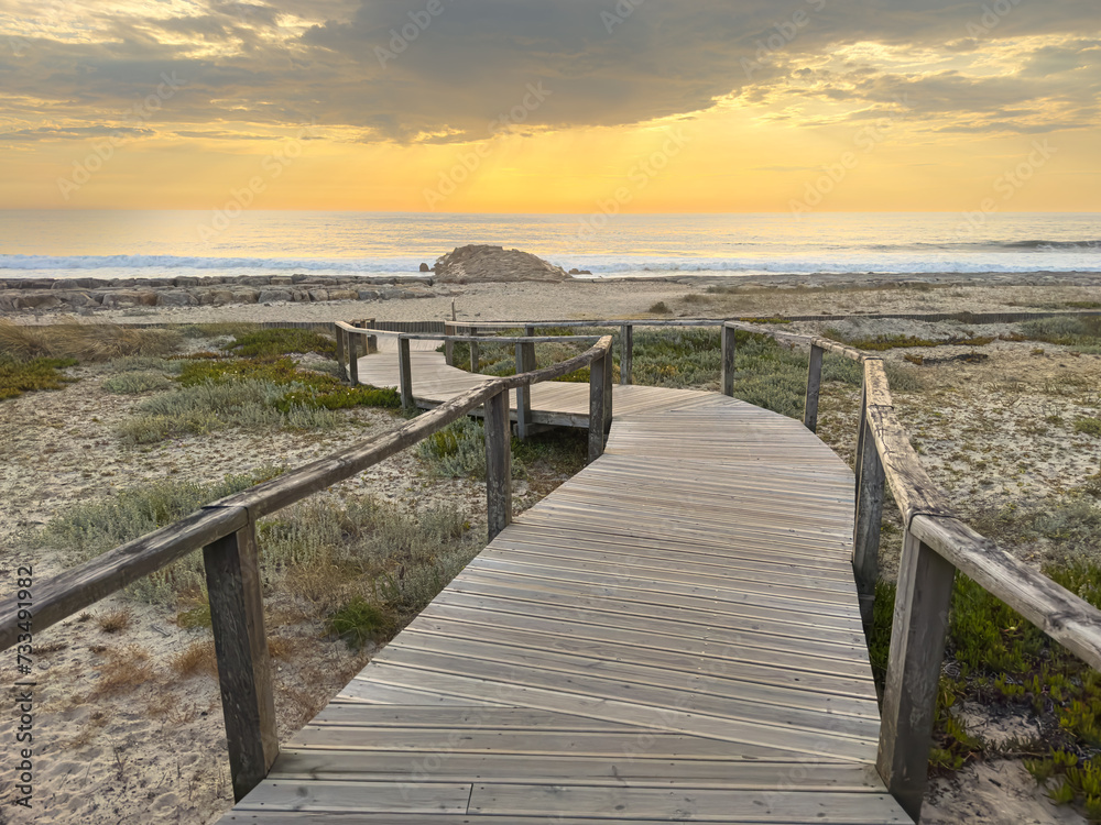 A wood pedestrian walkways, build over a sand dune that is used to give beach access in Furadouro beach, glows at sunset. Ovar, Aveiro, Portugal, Europe